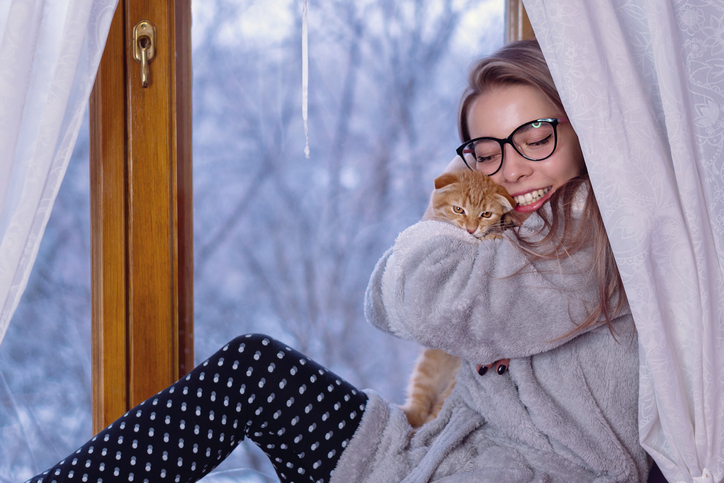 A woman holding a cat tight sitting next to a window