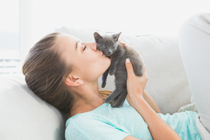 A woman kissing a kitten as she lays on a sofa
