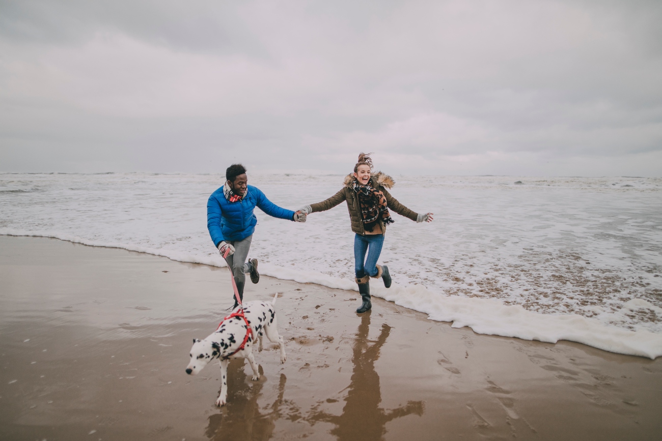 couple running on the beach with a dog