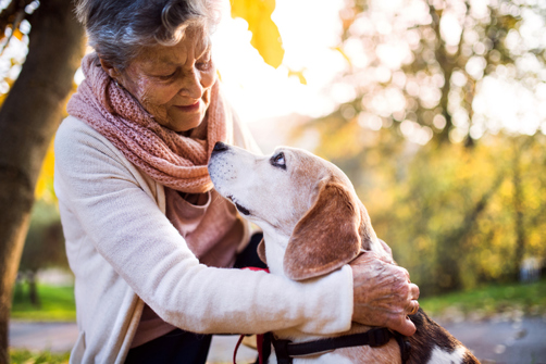 An elderly women hugging her dog whilst sitting down outside