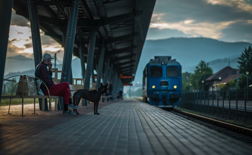 A man and his dog sitting on a train platform as a train comes in