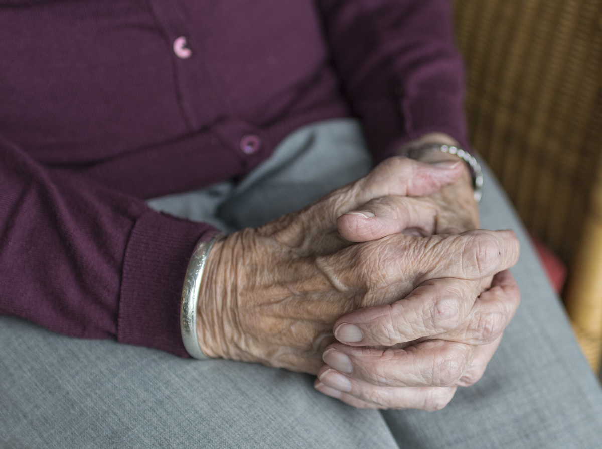 An elderly person siting in an armchair with her hands together