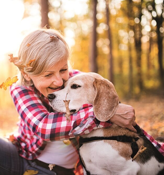 A woman sitting down in a woodland area hugging her dog