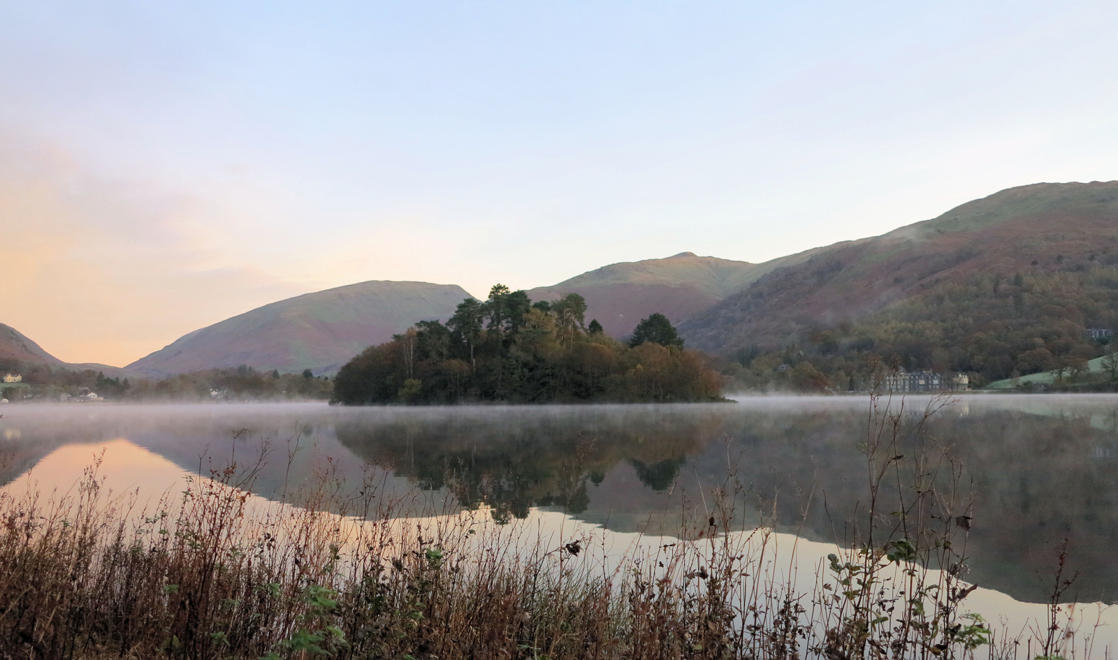 A misty lake in Grasmere surrounded by rolling green hills at dawn