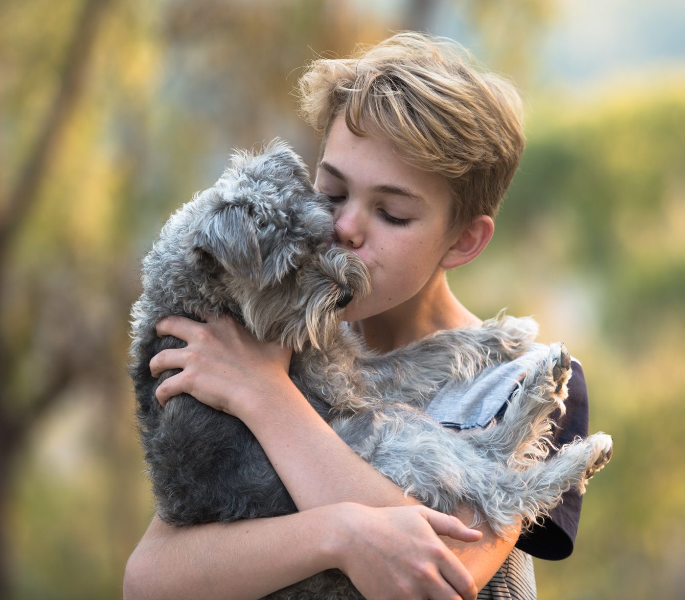 A boy holding a dog and giving it a kiss on the head