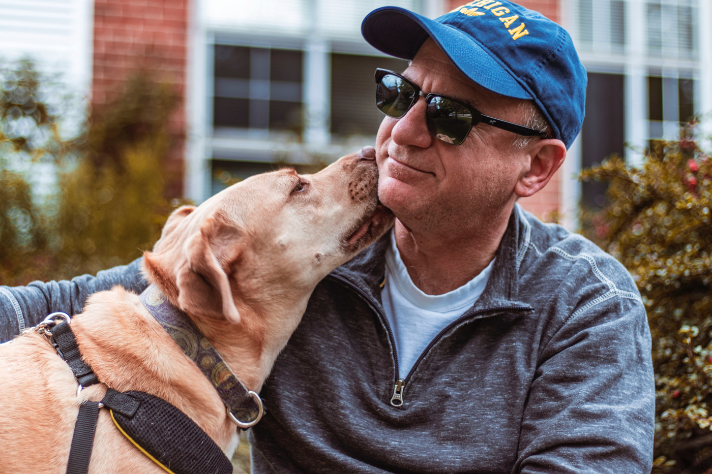 An dog licking its owners face in-front of a house